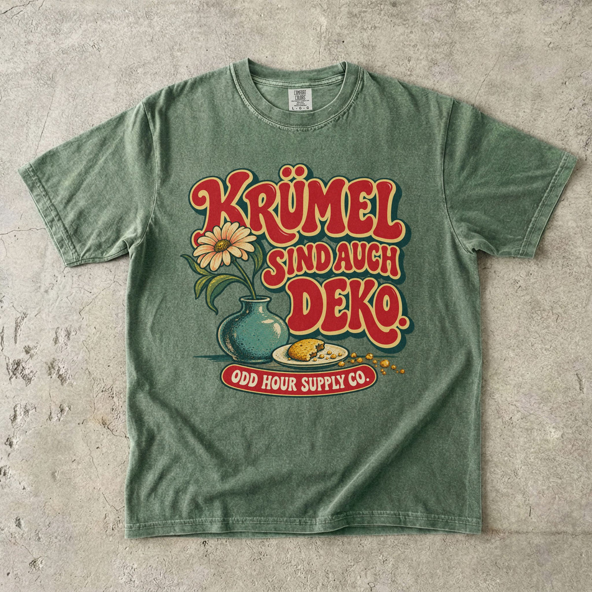 Comfort Colors 1717 T-Shirt in Moss mit dem Motiv „Krümel sind auch Deko“ mit Blumenvase, Vorderansicht