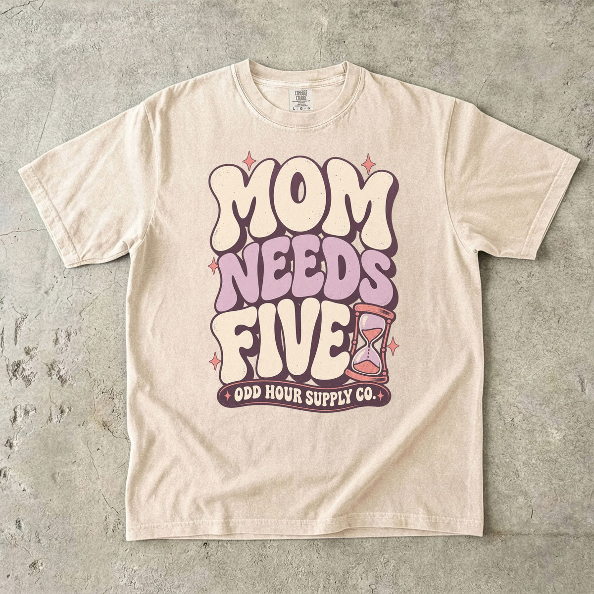 Comfort Colors 1717 T-Shirt in Ivory mit cremefarbener und fliederfarbener Mom Needs Five-Schrift, rosa Sternen und einer Sanduhr.