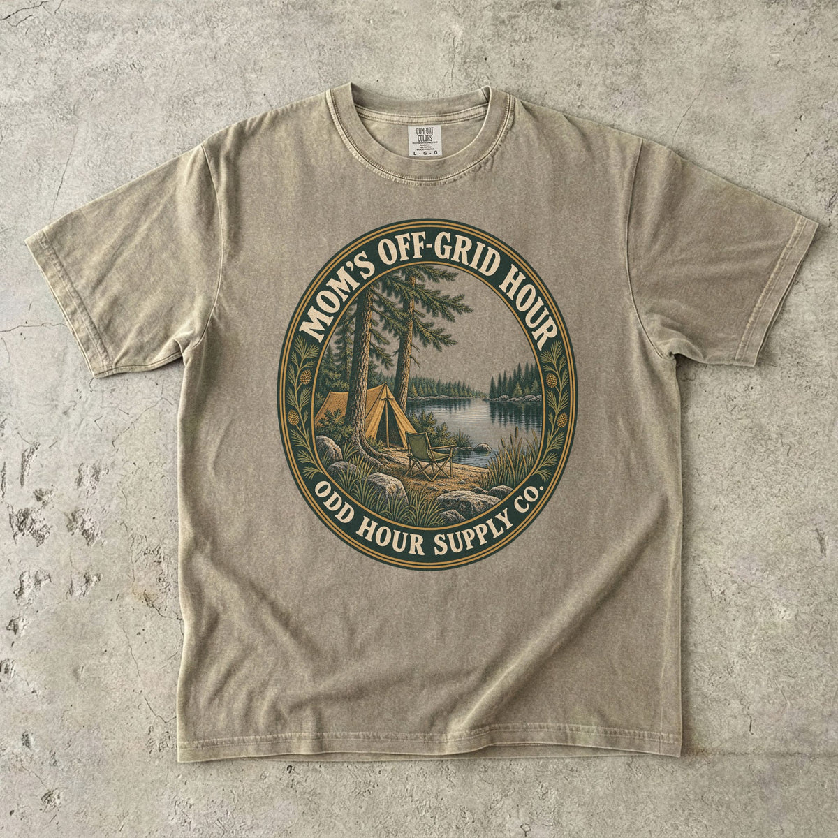 Comfort Colors 1717 T-Shirt in Khaki mit ovalem Mom’s Off-Grid Hour-Abzeichen, Zelt, Campingstuhl, Kiefern und See.