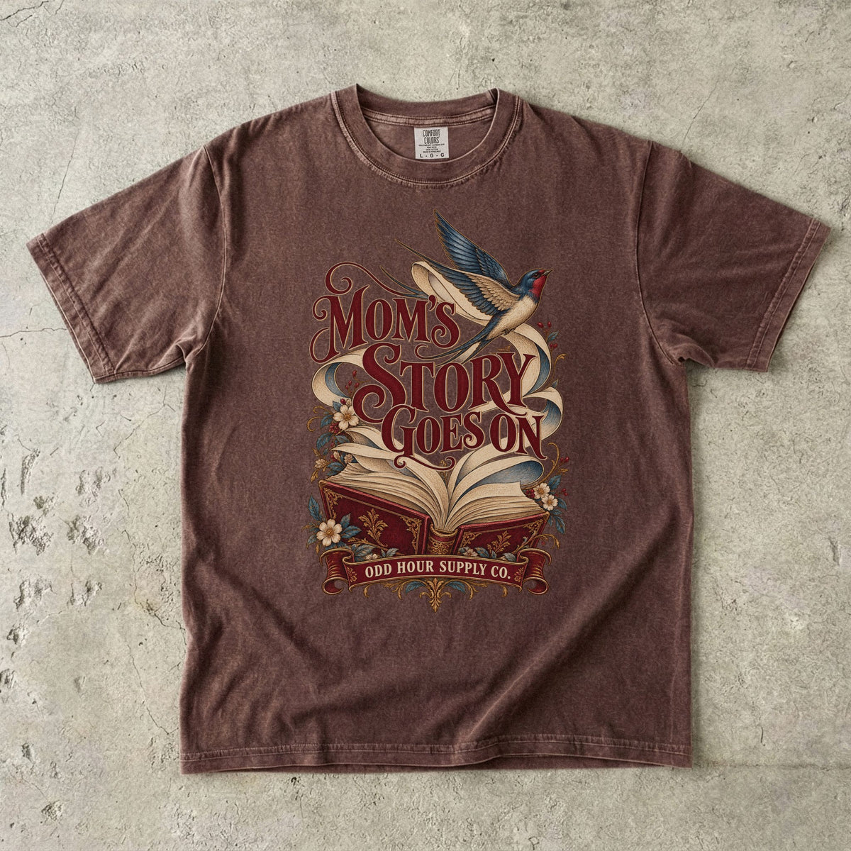 Comfort Colors 1717 T-Shirt in Espresso mit offenem rotem Buch, geschwungenen Seiten, fliegender Schwalbe, Blumen und Mom’s Story Goes On-Schrift.