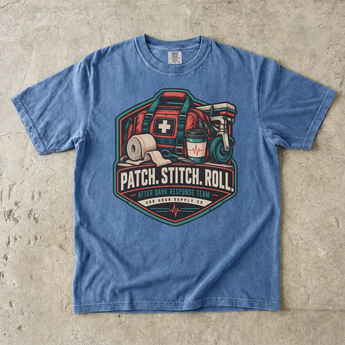 Comfort Colors 1717 T-Shirt in Washed Denim mit Patch Stitch Roll Badge, korallfarbener Notfalltasche, Verbänden, Kaffeebecher und Petrol-Akzenten.