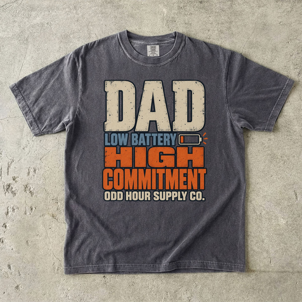 Comfort Colors 1717 T-Shirt in Pepper mit großer Dad Low Battery High Commitment-Schrift in Creme, Blau und Orange sowie fast leerem Batteriesymbol.