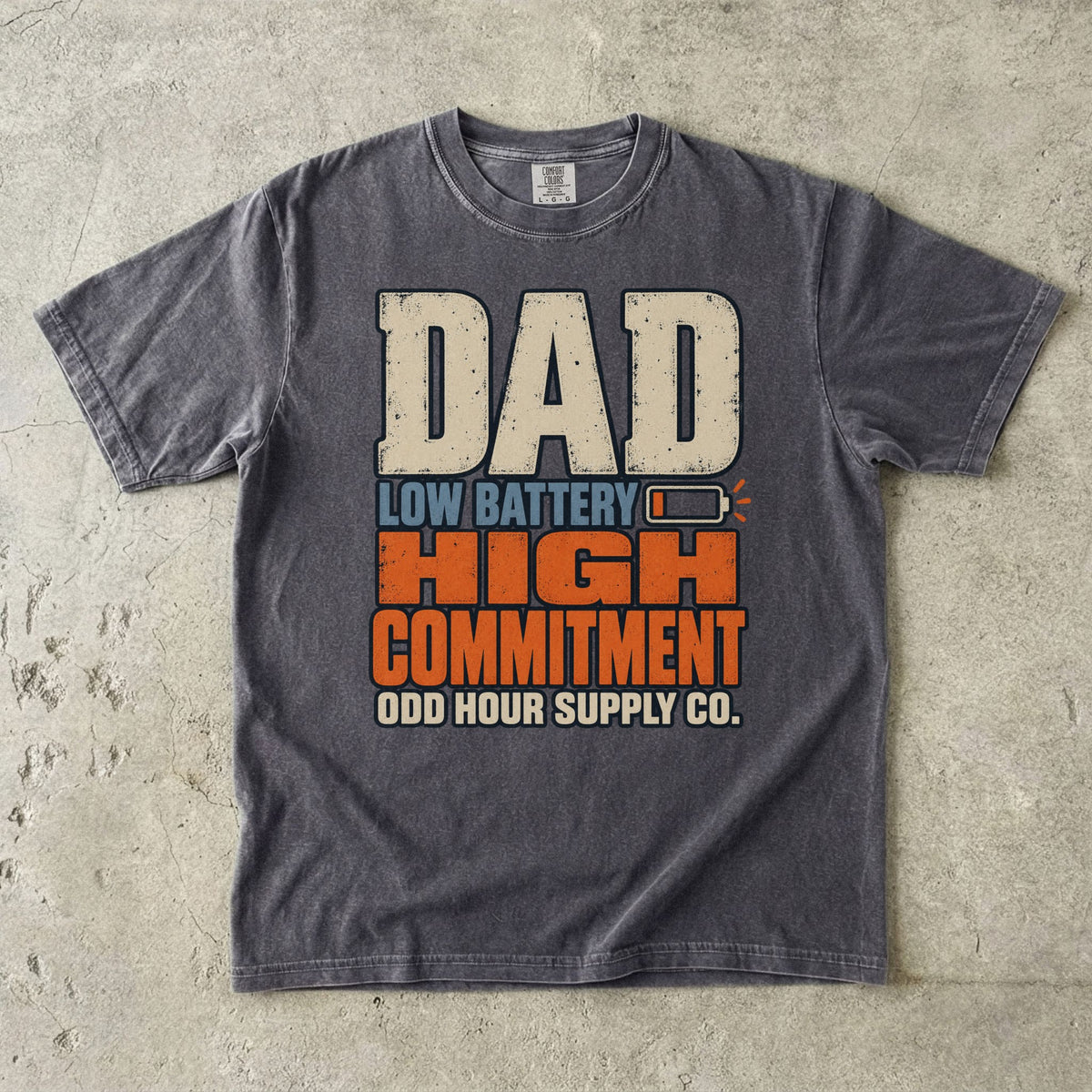 Comfort Colors 1717 T-Shirt in Pepper mit großer Dad Low Battery High Commitment-Schrift in Creme, Blau und Orange sowie fast leerem Batteriesymbol.