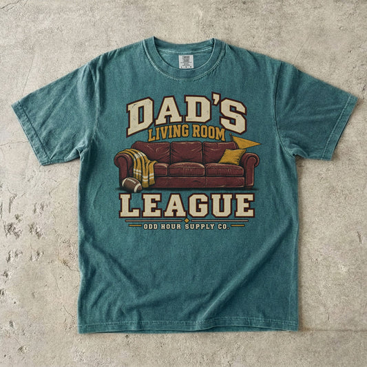 Comfort Colors 1717 T-Shirt in Blue Spruce mit rotbraunem Sofa, Football, gelber Decke und Dad’s Living Room League-Schrift.