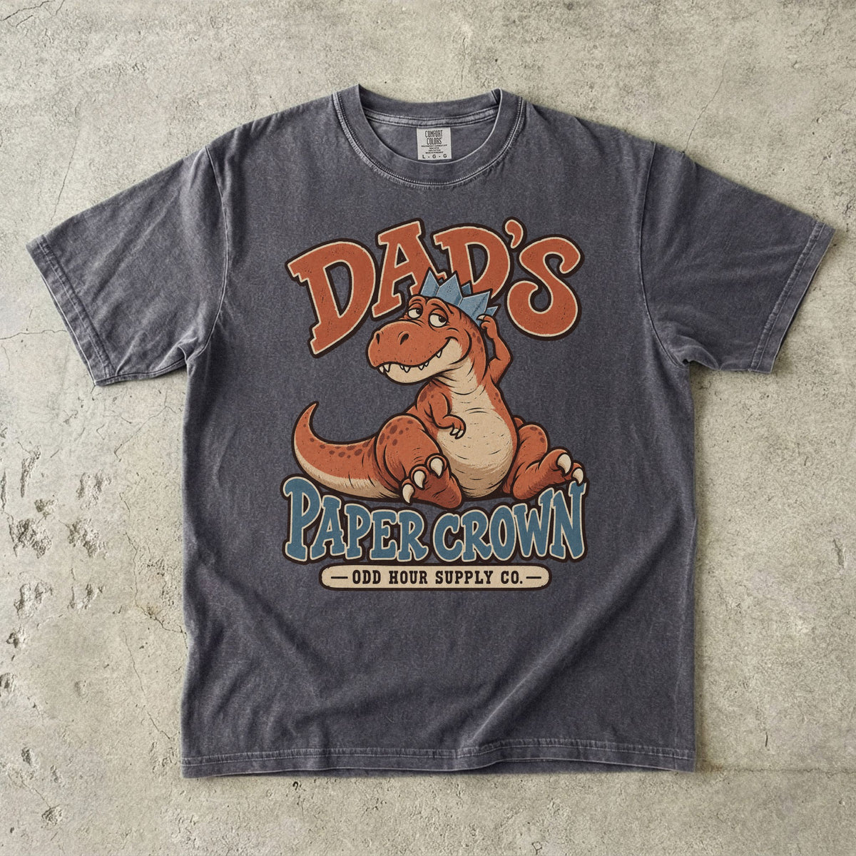 Comfort Colors 1717 T-Shirt in Pepper mit sitzendem orangefarbenem Dinosaurier, blauer Papierkrone und Dad’s Paper Crown-Schrift.