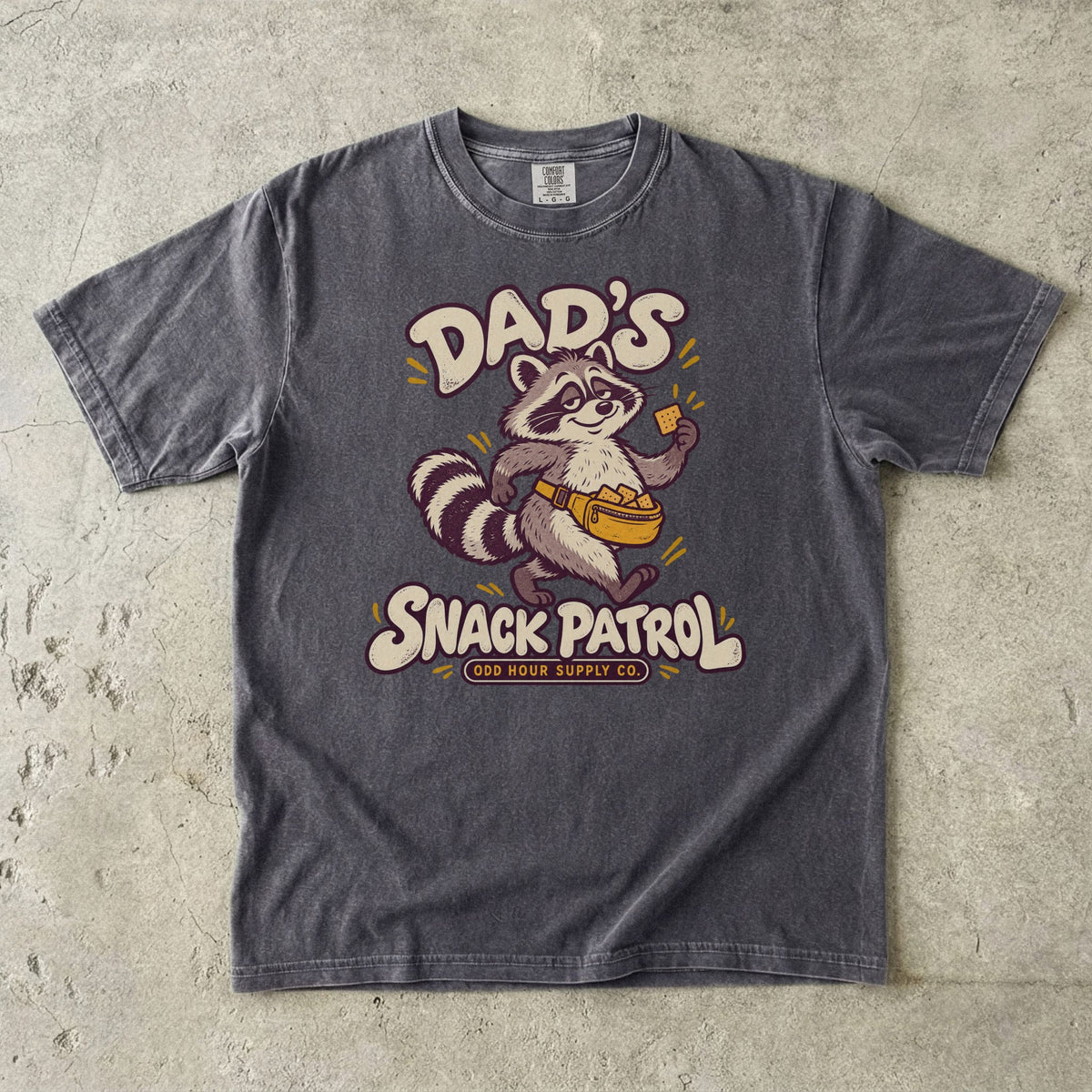 Comfort Colors 1717 T-Shirt in Pepper mit Waschbär, gelber Bauchtasche voller Cracker und cremefarbener Dad’s Snack Patrol-Schrift.