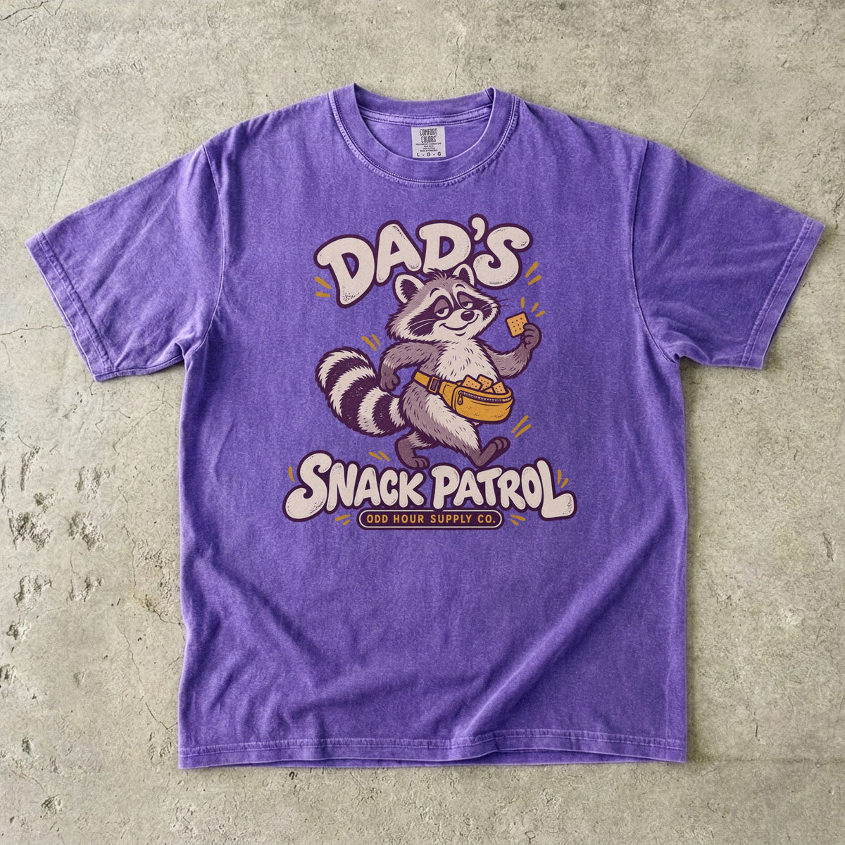 Comfort Colors 1717 T-Shirt in Violet mit Waschbär, gelber Bauchtasche voller Cracker und cremefarbener Dad’s Snack Patrol-Schrift.