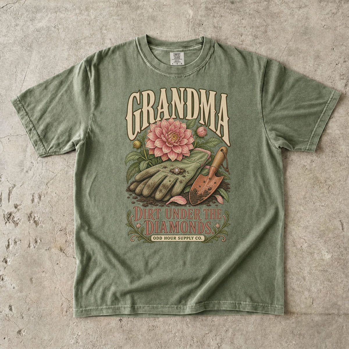 Comfort Colors 1717 T-Shirt in Hemp mit Gartenhandschuhen, Ring, rosa Dahlie, Pflanzkelle und der Aufschrift Grandma Dirt Under the Diamonds.