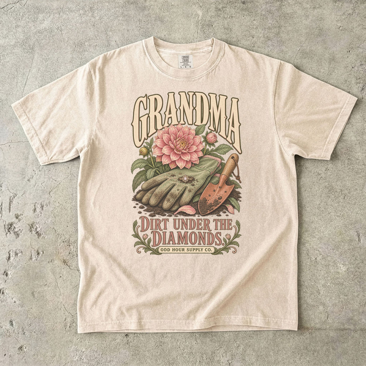 Comfort Colors 1717 T-Shirt in Ivory mit Gartenhandschuhen, Ring, rosa Dahlie, Pflanzkelle und der Aufschrift Grandma Dirt Under the Diamonds.