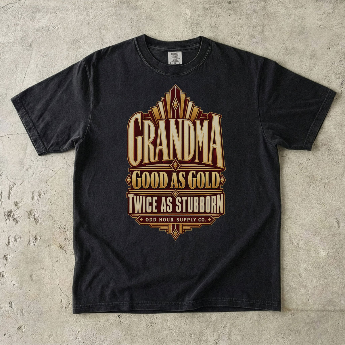 Comfort Colors 1717 T-Shirt in Black mit goldfarbenen geometrischen Linien und der Aufschrift Grandma Good as Gold Twice as Stubborn auf burgunderroter Fläche.