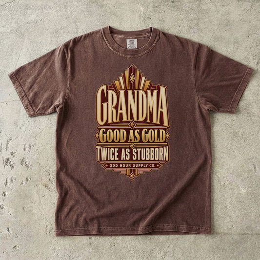 Comfort Colors 1717 T-Shirt in Espresso mit goldfarbenen geometrischen Linien und der Aufschrift Grandma Good as Gold Twice as Stubborn auf burgunderroter Fläche.