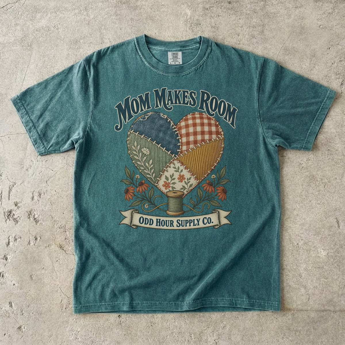 Comfort Colors 1717 T-Shirt in Blue Spruce mit Patchwork-Herz aus gemusterten Stoffstücken, Blumen, Garnrolle und Mom Makes Room-Schrift.