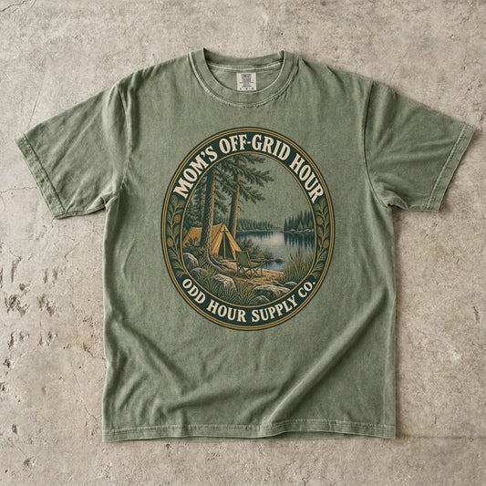 Comfort Colors 1717 T-Shirt in Hemp mit ovalem Mom’s Off-Grid Hour-Abzeichen, Zelt, Campingstuhl, Kiefern und See.