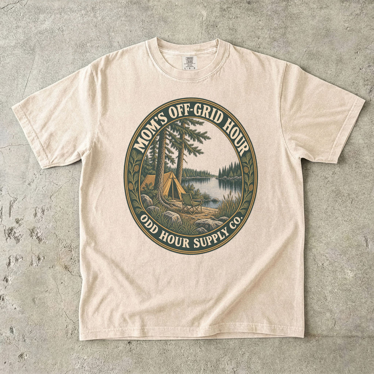Comfort Colors 1717 T-Shirt in Ivory mit ovalem Mom’s Off-Grid Hour-Abzeichen, Zelt, Campingstuhl, Kiefern und See.