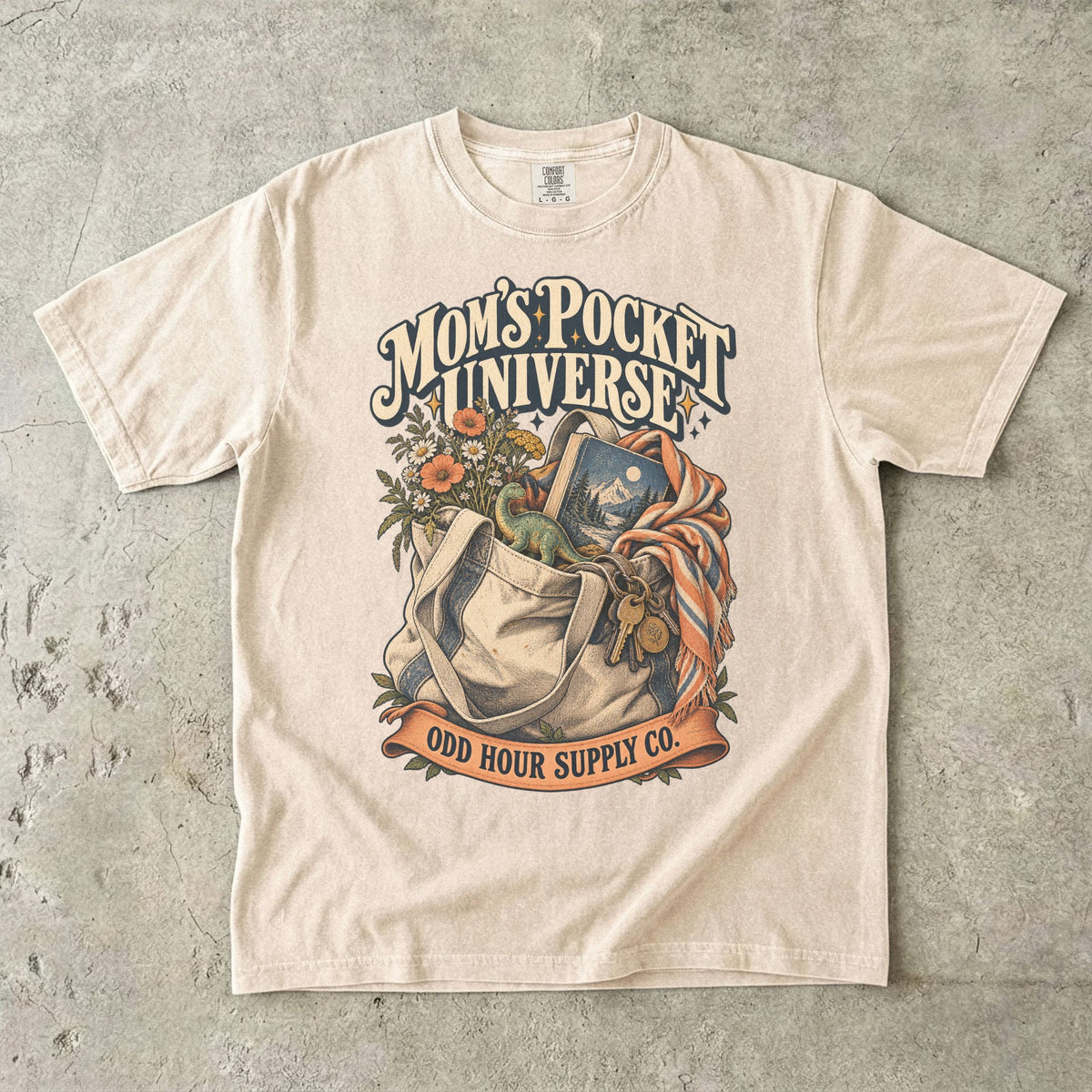 Comfort Colors 1717 T-Shirt in Ivory mit gefüllter Stofftasche, Blumen, Buch, Spielzeugdinosaurier, Schlüsseln und Mom’s Pocket Universe-Schrift.