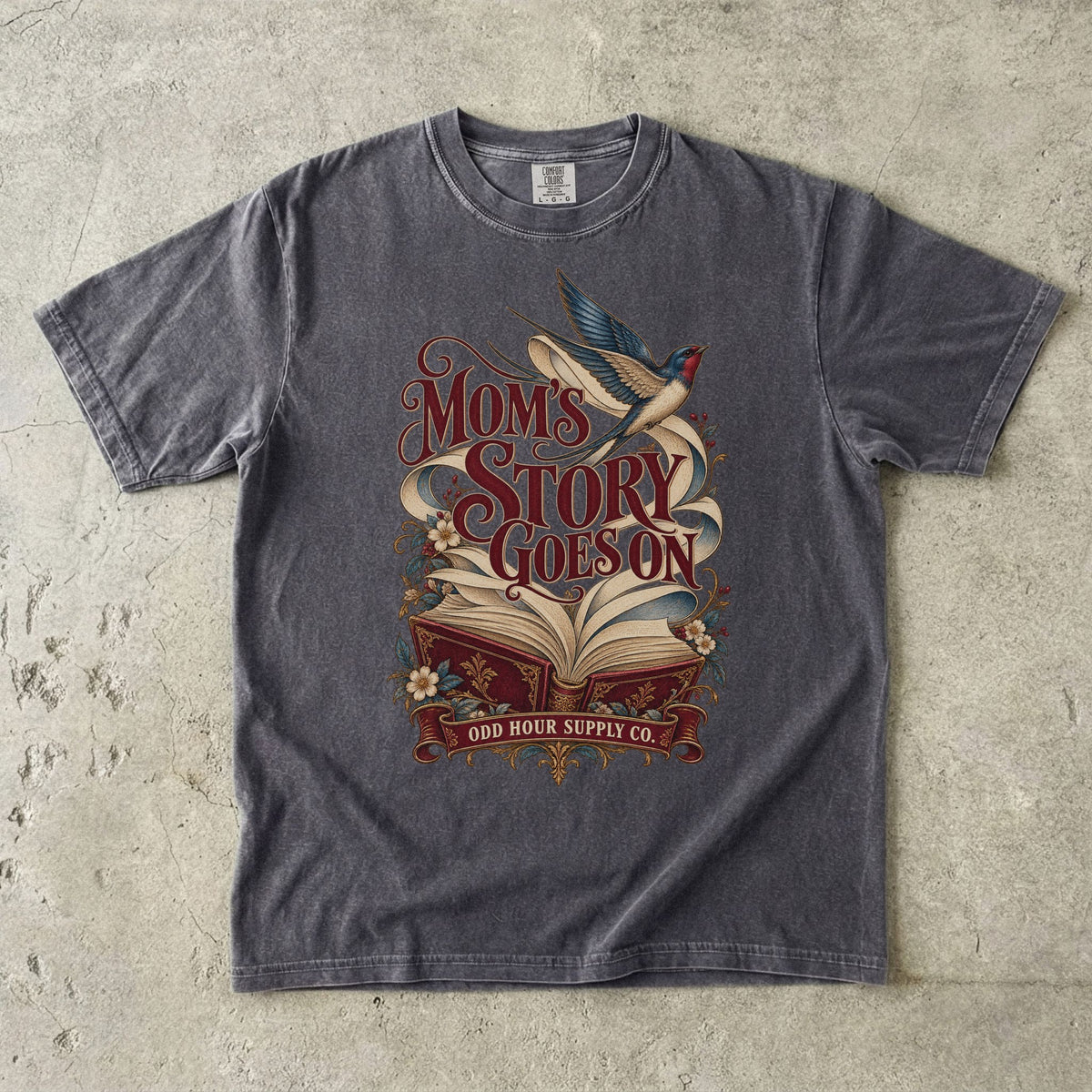 Comfort Colors 1717 T-Shirt in Pepper mit offenem rotem Buch, geschwungenen Seiten, fliegender Schwalbe, Blumen und Mom’s Story Goes On-Schrift.
