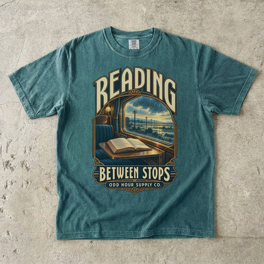 T-Shirt in Blue Spruce mit Zugfenster, offenem Buch und READING BETWEEN STOPS von Odd Hour Supply Co.