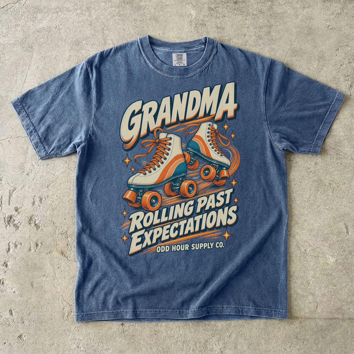 Comfort Colors 1717 T-Shirt in Denim mit cremefarbenen Rollschuhen mit orangefarbenen und türkisen Details und Grandma Rolling Past Expectations-Schrift.
