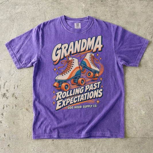 Comfort Colors 1717 T-Shirt in Violet mit cremefarbenen Rollschuhen mit orangefarbenen und türkisen Details und Grandma Rolling Past Expectations-Schrift.