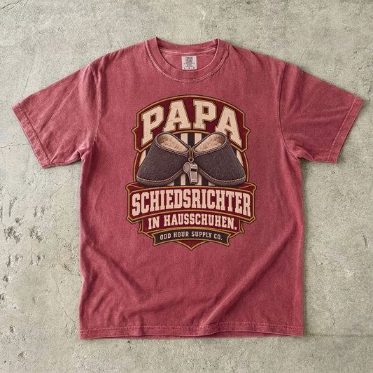 Comfort Colors 1717 T-Shirt in Brick: Wappen mit grauen Hausschuhen und silberner Trillerpfeife, darüber PAPA, darunter SCHIEDSRICHTER IN HAUSSCHUHEN. und ODD HOUR SUPPLY CO.