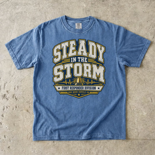 Comfort Colors 1717 T-Shirt in Washed Denim mit Steady in the Storm College-Motiv, gelber Rundumleuchte, Pulslinien und First Responder Division Schriftzug.