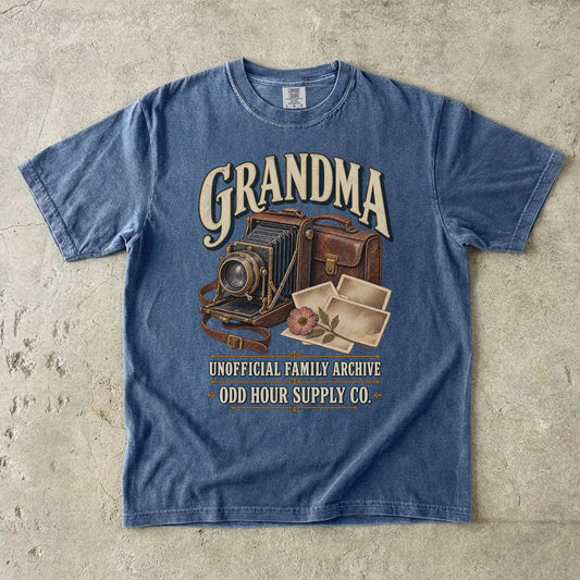 Comfort Colors 1717 T-Shirt in Denim mit alter Faltkamera, brauner Kameratasche, Fotoabzügen, Blüte und der Aufschrift Grandma Unofficial Family Archive.