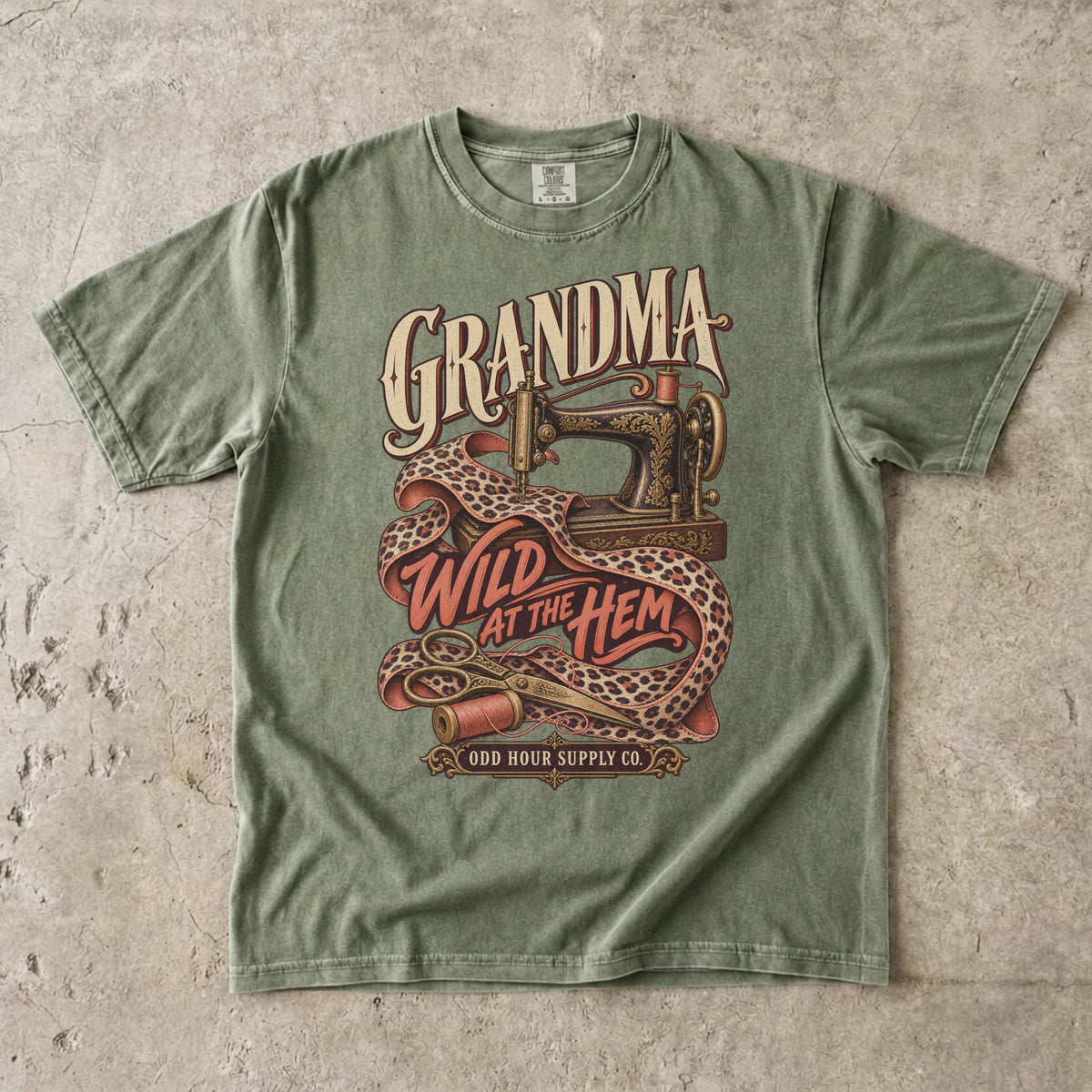 Comfort Colors 1717 T-Shirt in Hemp mit verzierter Nähmaschine, Stoff mit Leopardenmuster, Garnrollen und der Aufschrift Grandma Wild at the Hem.