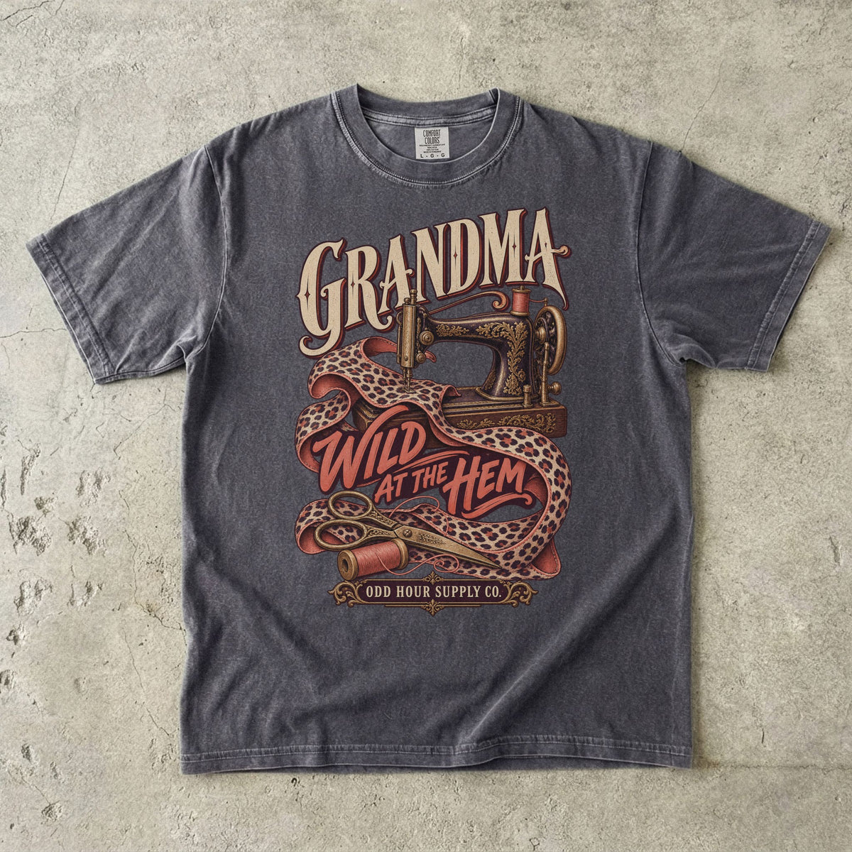 Comfort Colors 1717 T-Shirt in Pepper mit verzierter Nähmaschine, Stoff mit Leopardenmuster, Garnrollen und der Aufschrift Grandma Wild at the Hem.